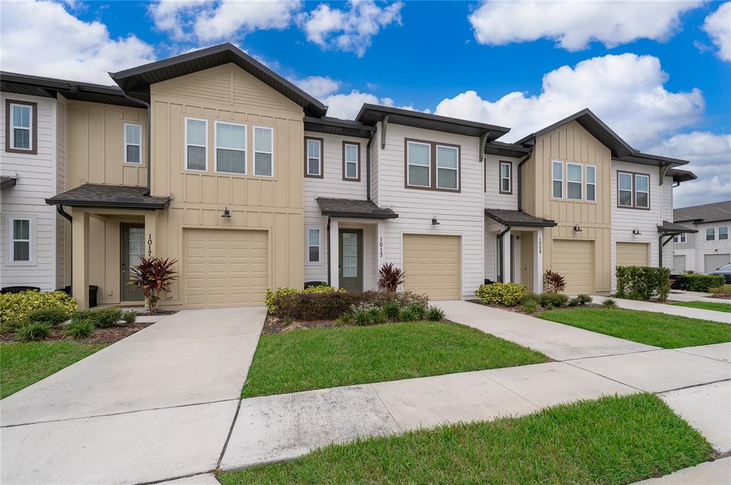 A row of multi-story townhomes with beige and white siding, garages, and concrete driveways — 1013 PLANTATION LANE, DAVENPORT, FL