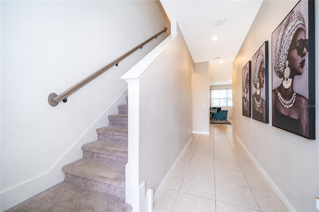 A carpeted staircase with a wooden handrail leads up beside a tiled hallway with artwork — 1013 PLANTATION LANE, DAVENPORT, FL