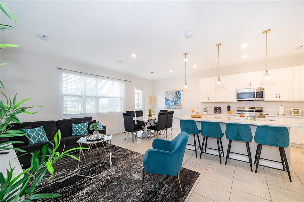 An open-concept kitchen and living area features white cabinetry, teal bar stools, and tile flooring — 1013 PLANTATION LANE, DAVENPORT, FL