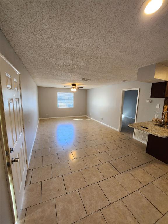 An open-concept living area features light-colored tile flooring, a ceiling fan, and a kitchen counter — 626 GOLDEN RAINTREE PLACE UNIT 626, BRANDON, FL