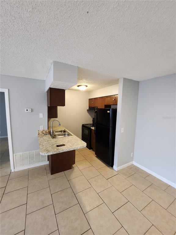 A kitchen features a granite-topped peninsula, dark wood cabinets, black appliances, and tiled flooring — 626 GOLDEN RAINTREE PLACE UNIT 626, BRANDON, FL