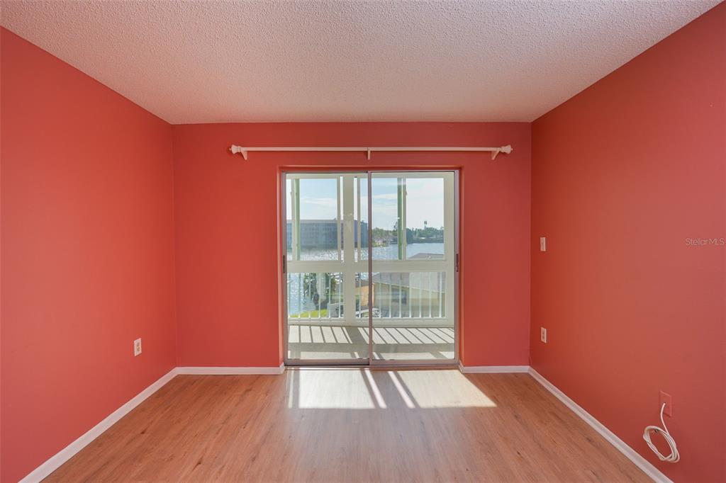 An empty bedroom with coral-colored walls, light wood-look flooring, and a sliding glass door — 3607 LAKE BAYSHORE DRIVE UNIT 312, BRADENTON, FL