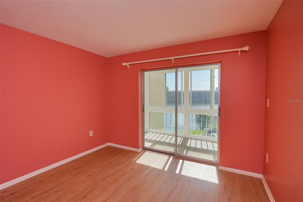An empty room with coral-colored walls, light wood flooring, and a sliding glass balcony door — 3607 LAKE BAYSHORE DRIVE UNIT 312, BRADENTON, FL