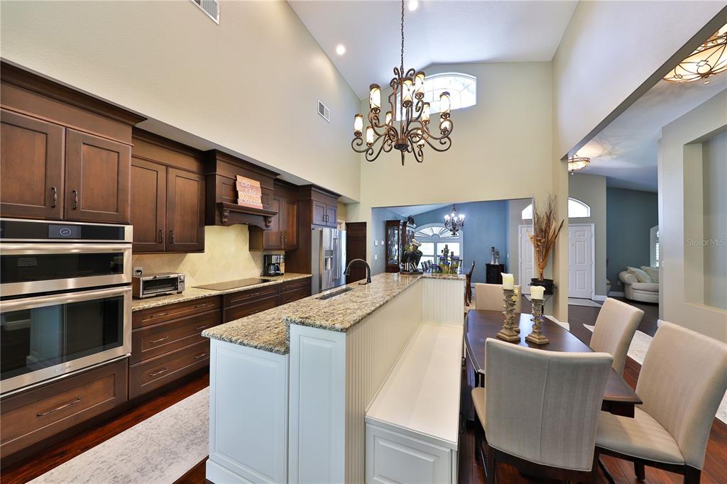 A kitchen with dark wood cabinets, granite countertops, and a white island with built-in seating — 2578 EKANA DRIVE, OVIEDO, FL