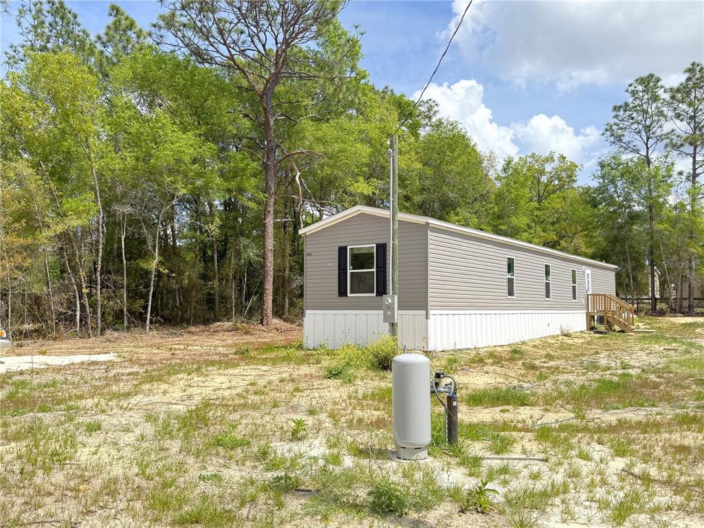 A single-story manufactured home sits on a sandy lot with a propane tank nearby — 4951 NE 141ST AVENUE, WILLISTON, FL