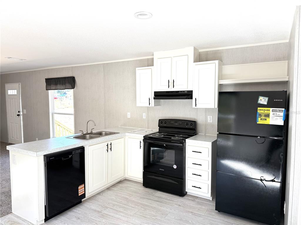 A kitchen features white cabinets, black appliances, a sink, and light-colored wood-look flooring — 4951 NE 141ST AVENUE, WILLISTON, FL