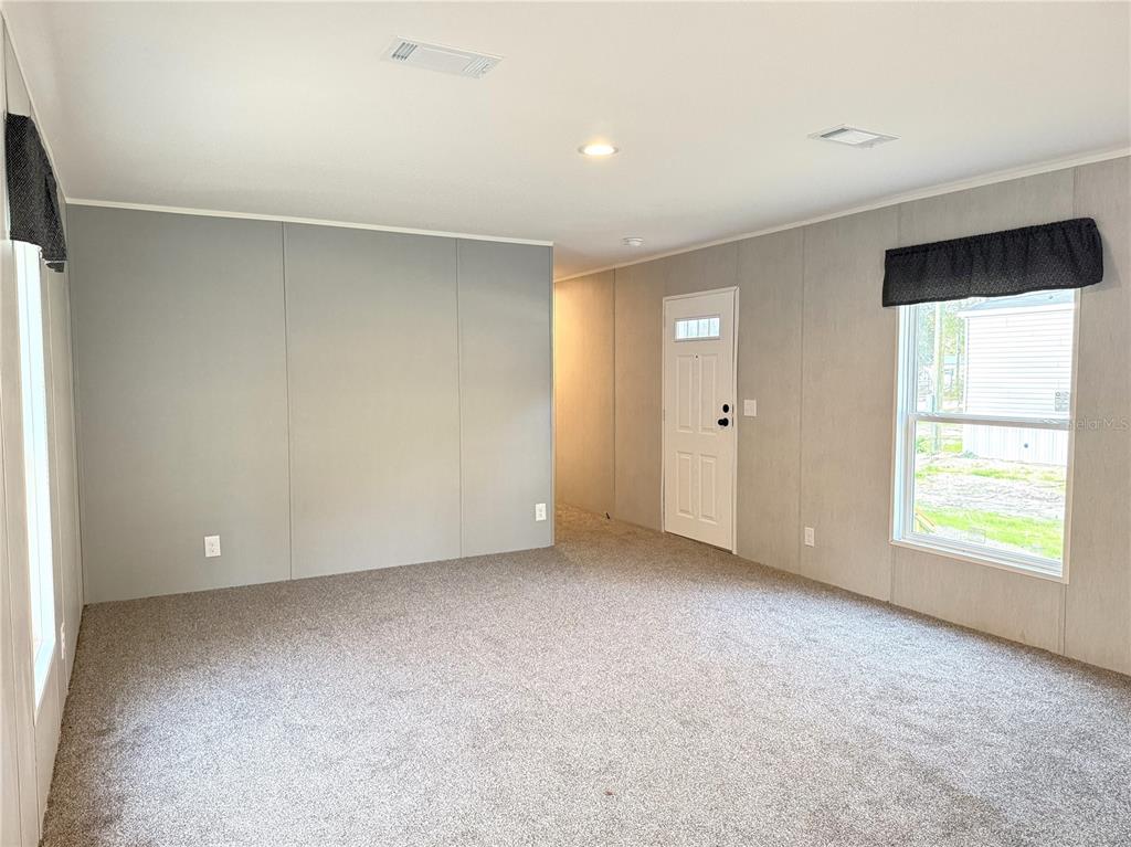An empty living room features gray paneled walls, beige carpeting, and a white entry door — 4951 NE 141ST AVENUE, WILLISTON, FL
