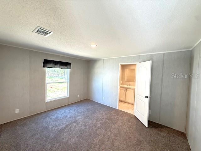 A bedroom with grey paneled walls, brown carpet, and an open door to a bathroom — 4951 NE 141ST AVENUE, WILLISTON, FL