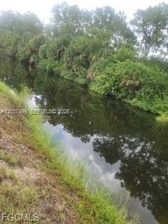 A narrow canal flows between a grassy bank and a line of dense trees — 439 Naples AVE S, Lehigh Acres FL 33974, LEHIGH ACRES, FL