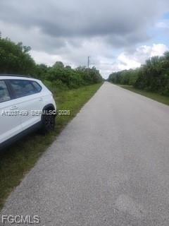 A white SUV is parked on the shoulder of a paved road bordered by trees — 439 Naples AVE S, Lehigh Acres FL 33974, LEHIGH ACRES, FL