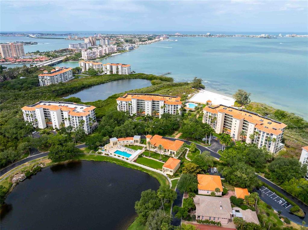 An aerial view shows several multi-story apartment buildings situated near a lake and the ocean — 4737 DOLPHIN CAY LANE S UNIT 407, ST PETERSBURG, FL