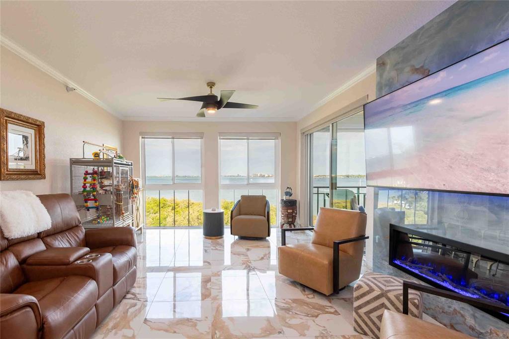A living room features marble floors, a fireplace, a television, and a view of water — 4737 DOLPHIN CAY LANE S UNIT 407, ST PETERSBURG, FL