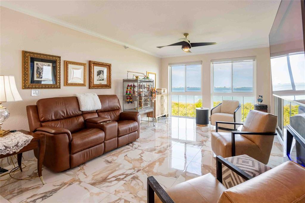 A living room with brown leather furniture, marble-look tile floors, and a waterfront view — 4737 DOLPHIN CAY LANE S UNIT 407, ST PETERSBURG, FL