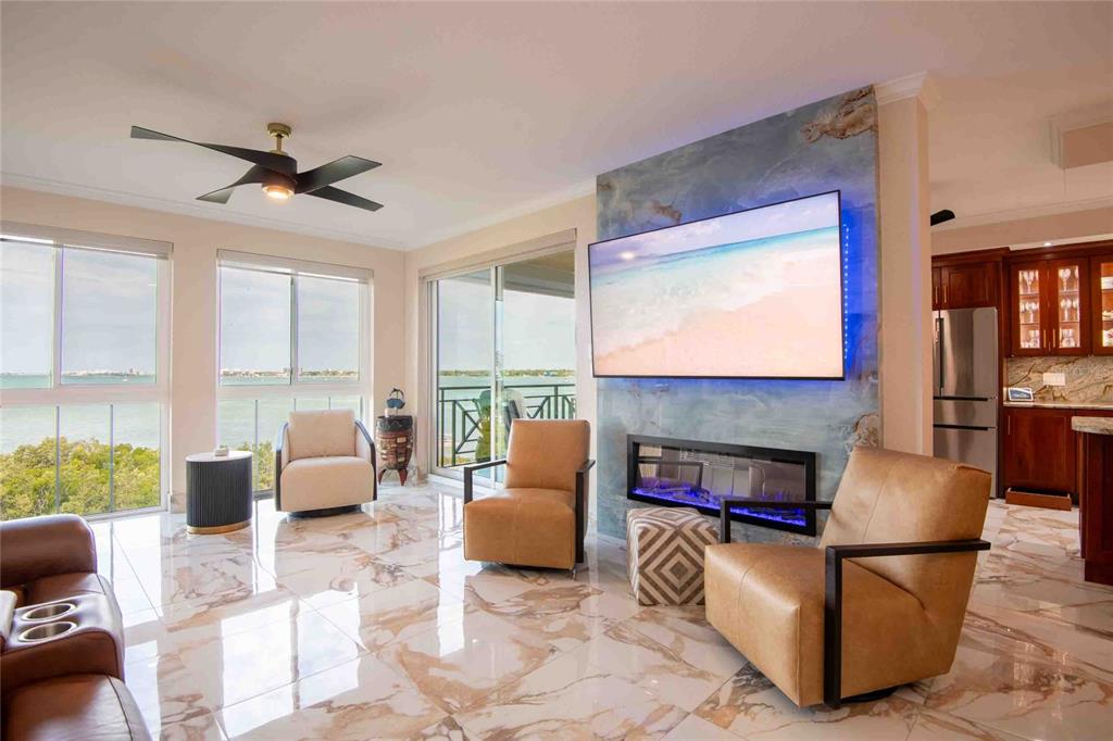 A living room features marble floors, a wall-mounted television, a fireplace, and waterfront views — 4737 DOLPHIN CAY LANE S UNIT 407, ST PETERSBURG, FL