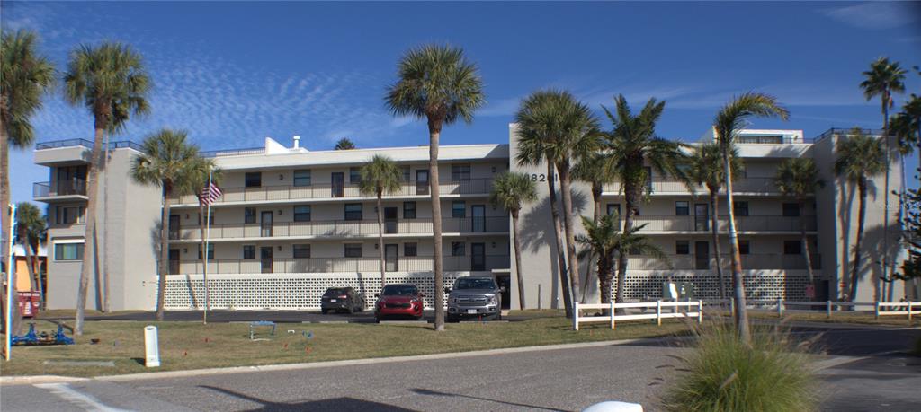A three-story apartment building with a white facade, palm trees, and a parking lot — 18201 GULF BOULEVARD UNIT 201, REDINGTON SHORES, FL