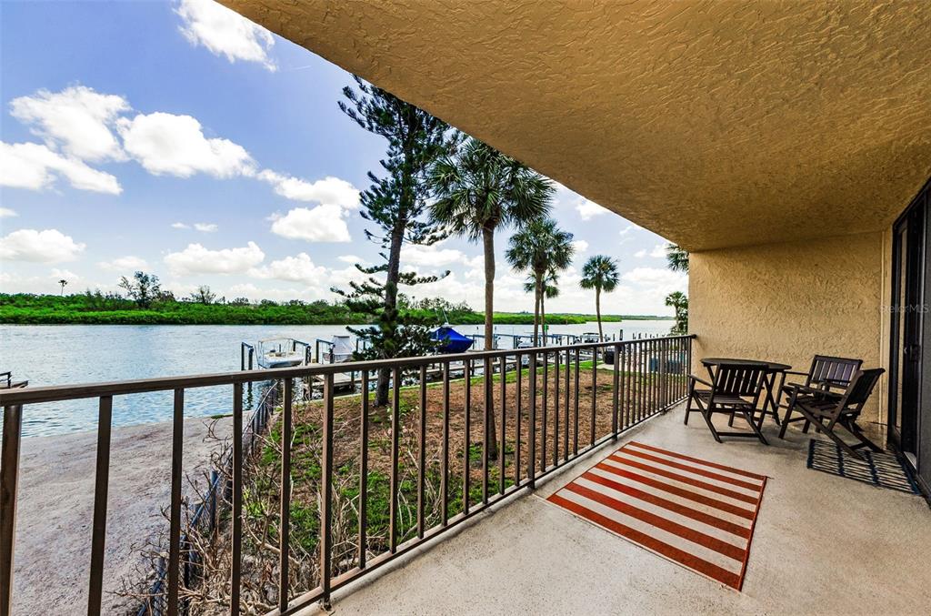A covered balcony overlooks a waterfront area with a boat dock and palm trees — 18201 GULF BOULEVARD UNIT 201, REDINGTON SHORES, FL