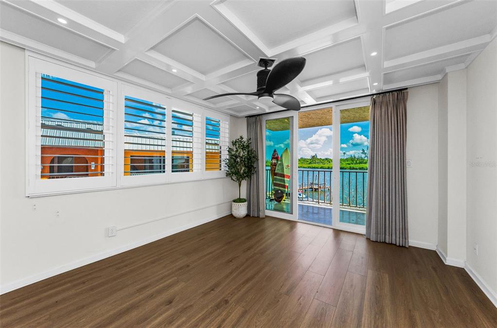 An empty room features wood-look flooring, a coffered ceiling, plantation shutters, and a balcony view — 18201 GULF BOULEVARD UNIT 201, REDINGTON SHORES, FL