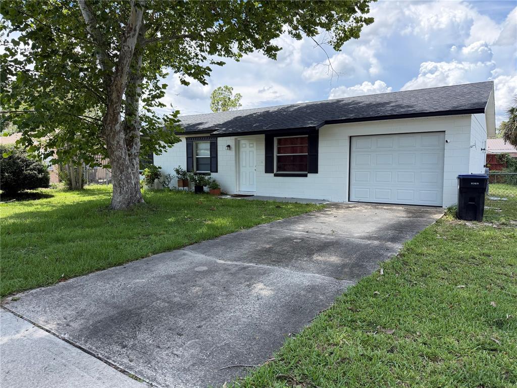 A single-story white house with a black roof, a garage, and a concrete driveway — 14109 NEWCOMB AVENUE, ORLANDO, FL