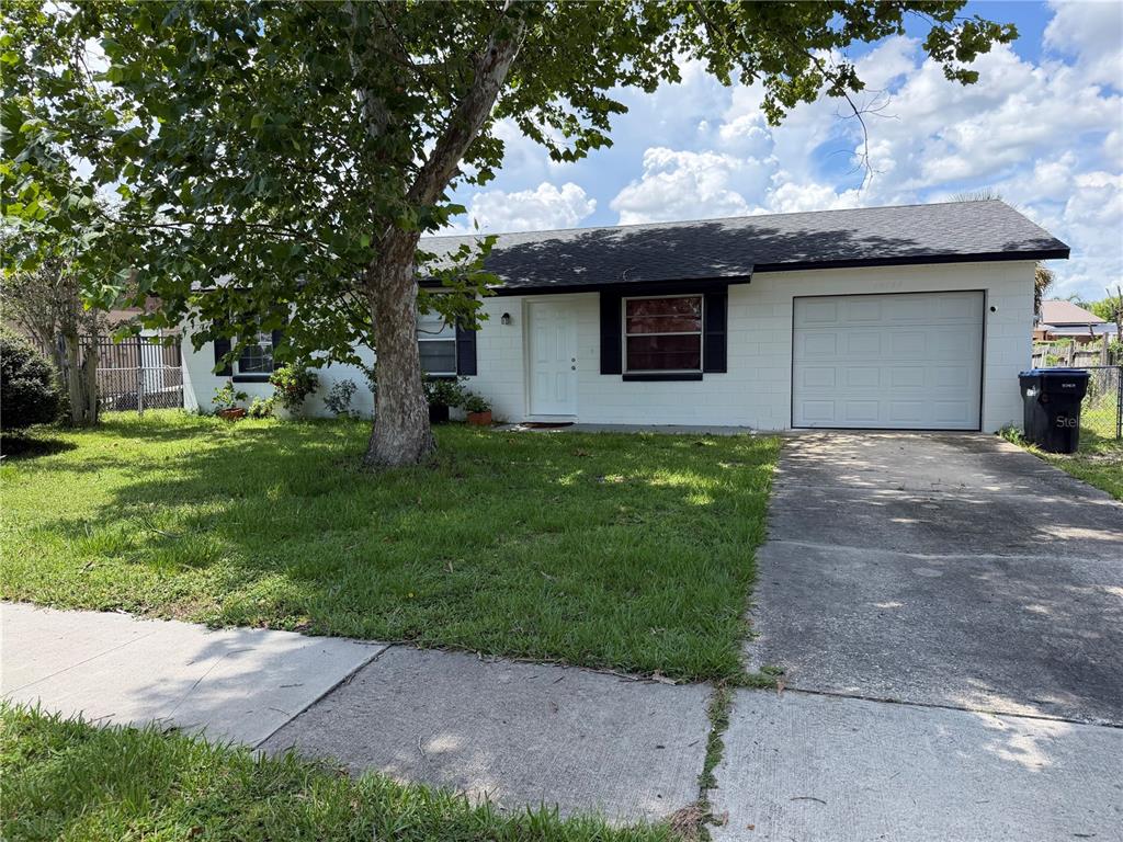 A single-story white house with a black roof, a front lawn, and an attached garage — 14109 NEWCOMB AVENUE, ORLANDO, FL