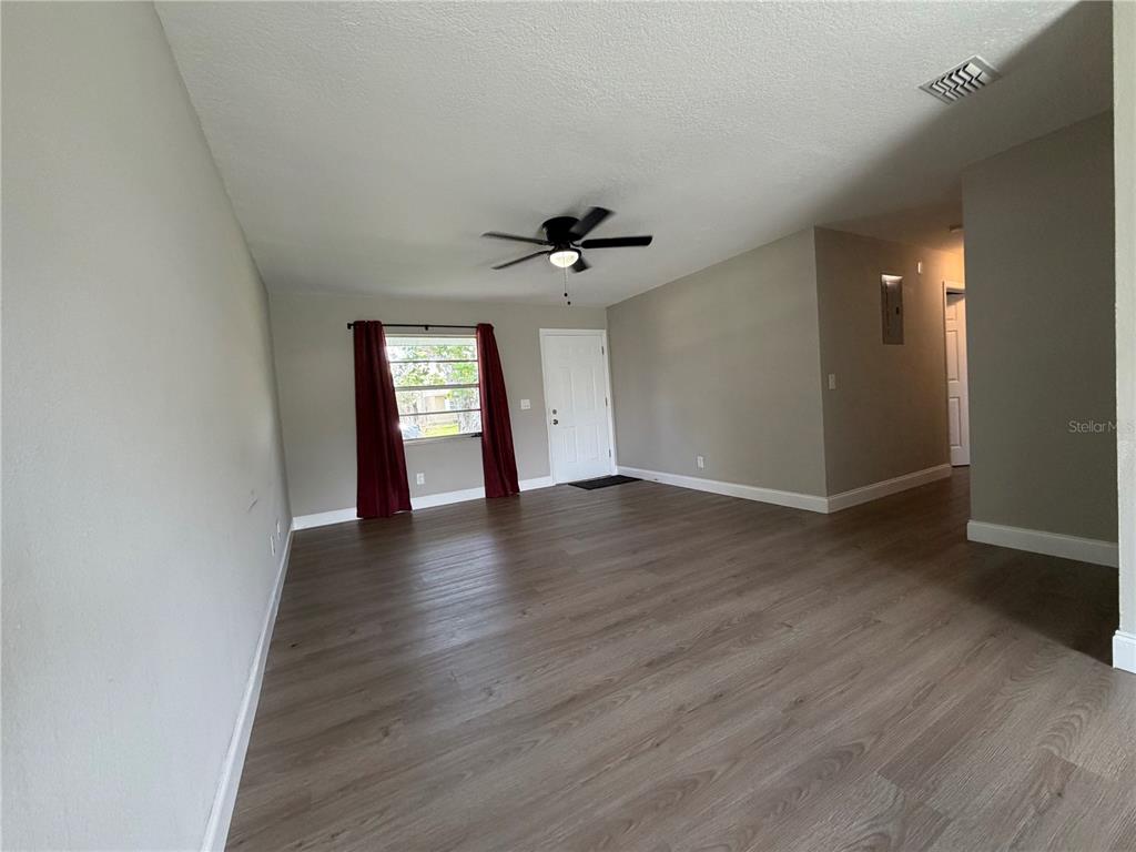 An empty living room features light-colored walls, wood-look flooring, a ceiling fan, and a window — 14109 NEWCOMB AVENUE, ORLANDO, FL