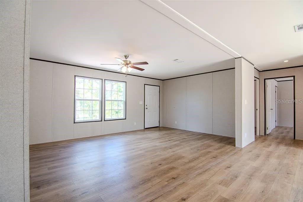 An open living area features light-colored walls, wood-look flooring, a ceiling fan, and a doorway — 19732 NW 280TH STREET, OKEECHOBEE, FL
