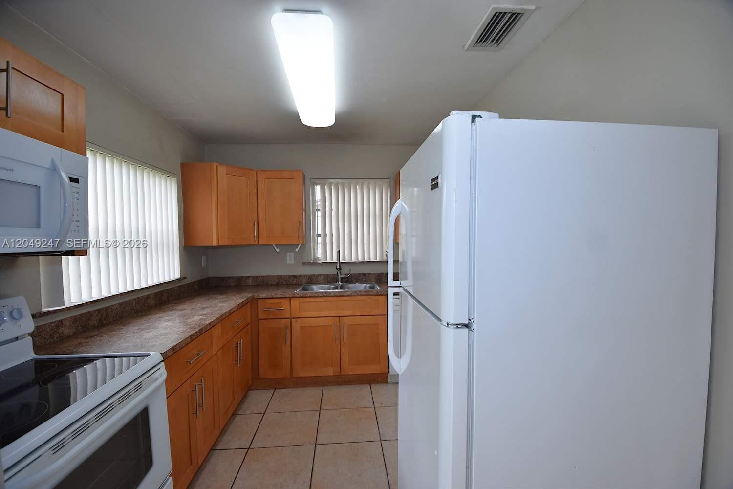 A kitchen features light wood cabinets, laminate countertops, white appliances, and beige tile flooring — MIAMI, FL
