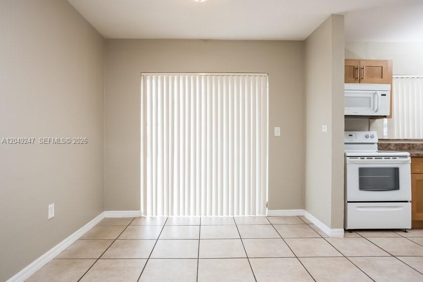 A dining area with tile flooring and vertical blinds leads to a kitchen with white appliances — MIAMI, FL