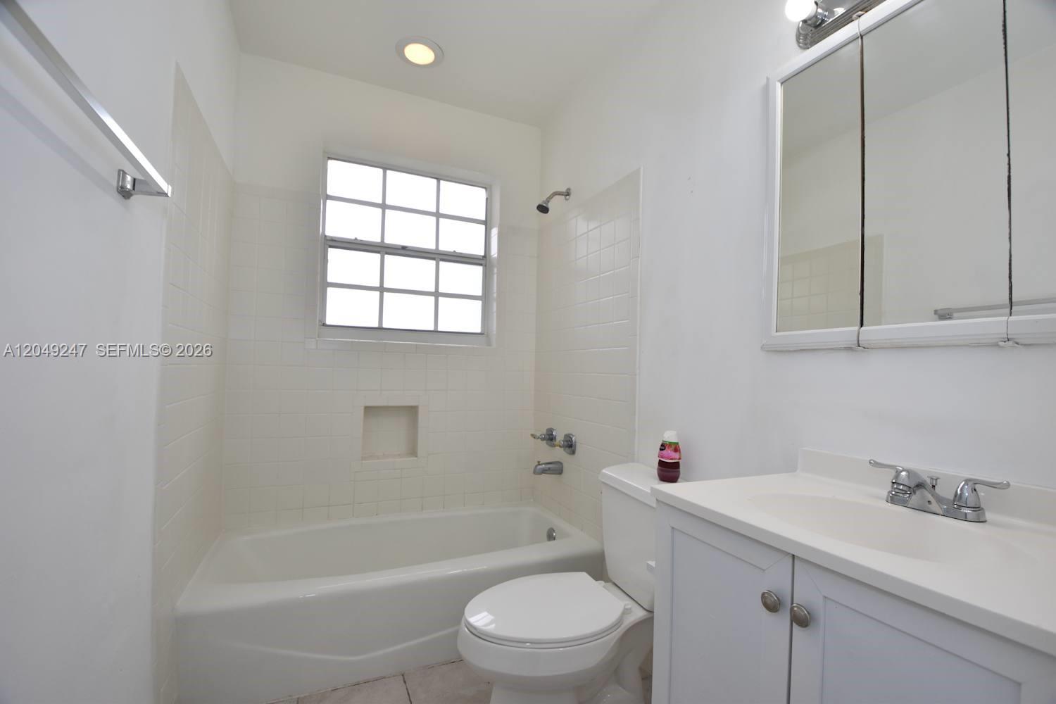 A bathroom features a white vanity, a toilet, and a bathtub with tiled walls — MIAMI, FL