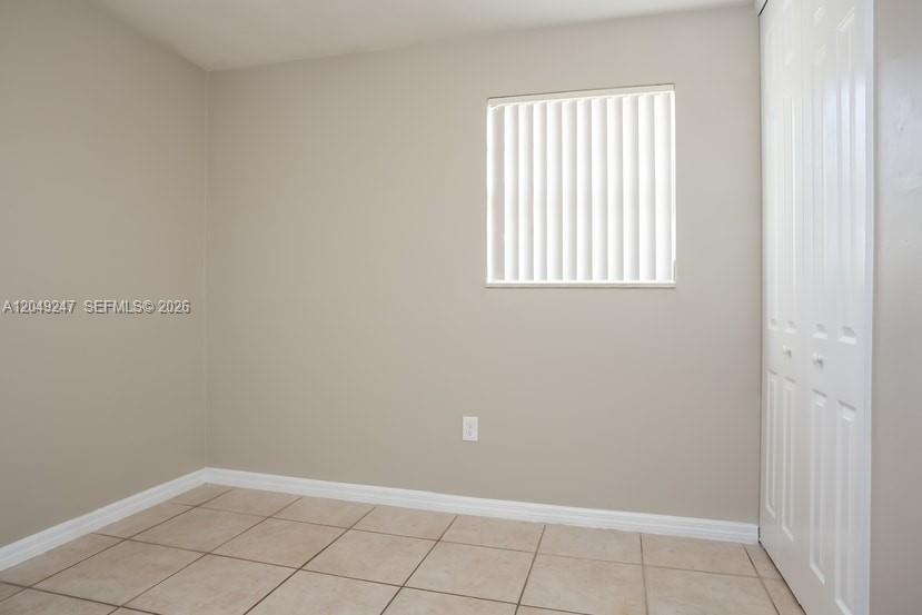 An empty room with beige walls, tile flooring, a window with blinds, and a closet — MIAMI, FL
