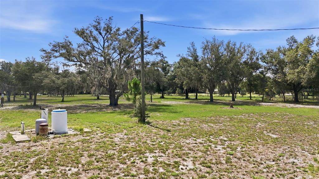 A grassy lot features a utility well system in the foreground and several large trees — 6096 NW CUL DE SAC ROAD, ARCADIA, FL