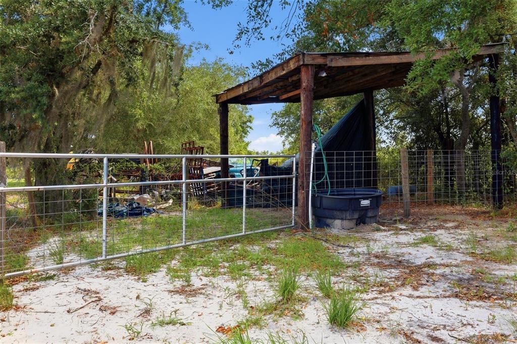 A metal gate opens to a sandy area with a covered shelter and water trough — 6096 NW CUL DE SAC ROAD, ARCADIA, FL