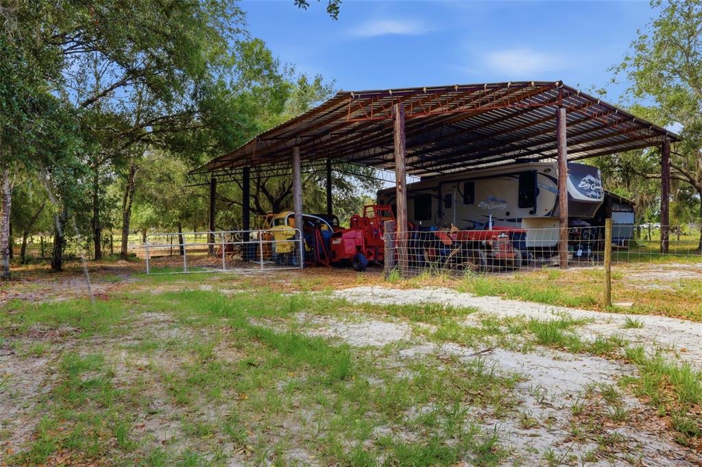 A large metal-roofed carport shelters a recreational vehicle and farm equipment on a rural lot — 6096 NW CUL DE SAC ROAD, ARCADIA, FL