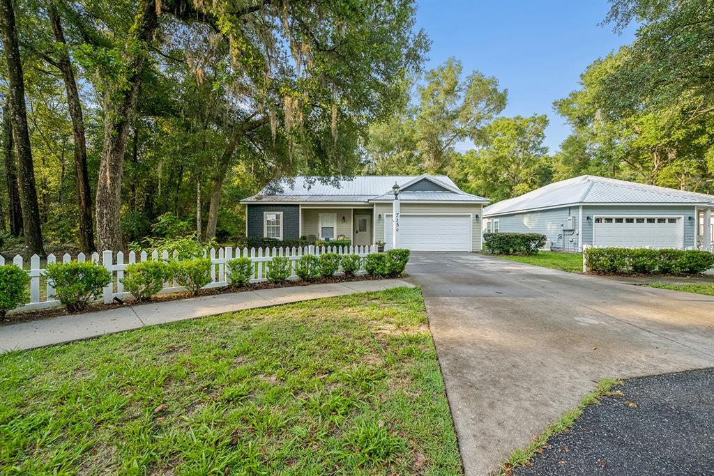 A single-story house with a white picket fence, a concrete driveway, and surrounding trees — 7250 CARDINAL TRAIL, FANNING SPRINGS, FL