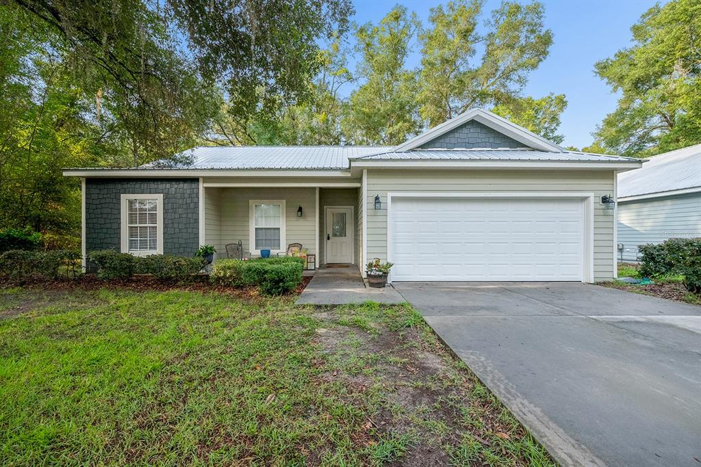 A single-story house with a metal roof, light siding, stone accents, and a two-car garage — 7250 CARDINAL TRAIL, FANNING SPRINGS, FL