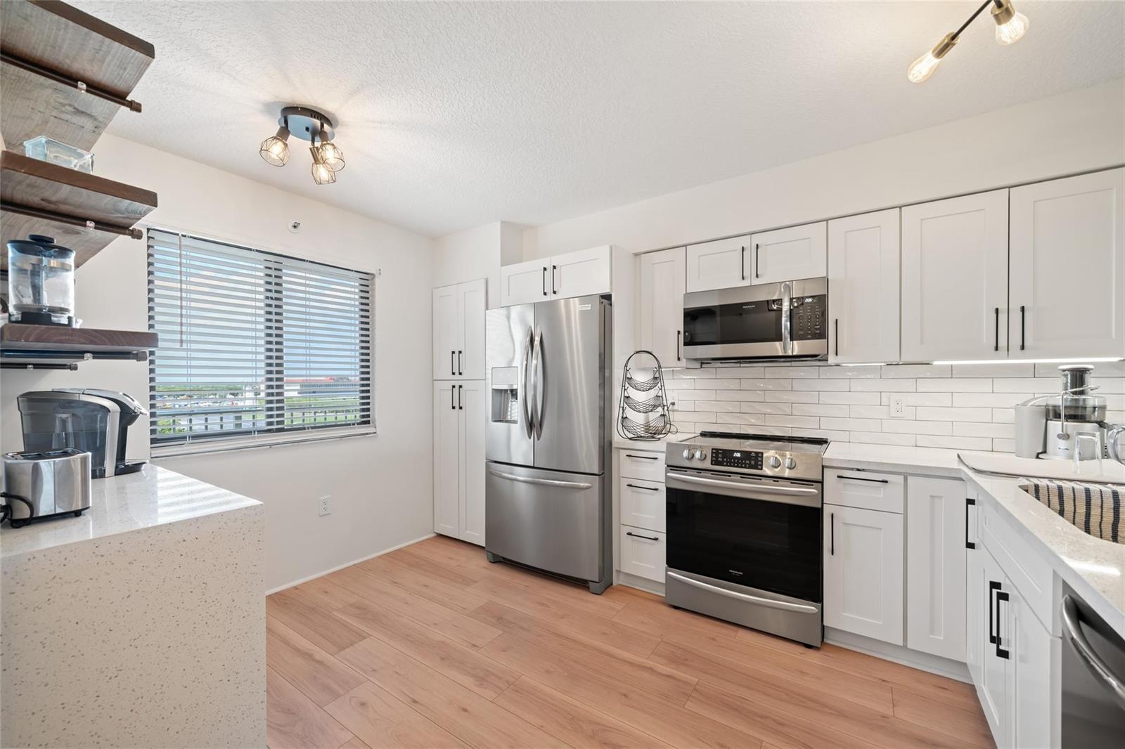 A modern kitchen features white cabinets, stainless steel appliances, quartz countertops, and light wood flooring — 2240 N Cypress Bend Drive # 802, Pompano Beach FL 33069, POMPANO BEACH, FL