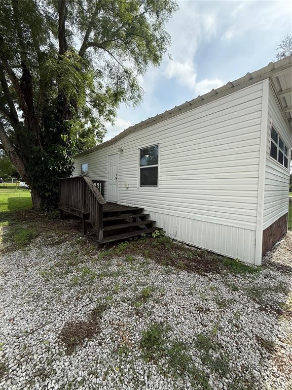 The exterior of a white mobile home features a wooden deck with stairs and gravel ground — 37412 CARRINGER RD UNIT 37412, DADE CITY, FL