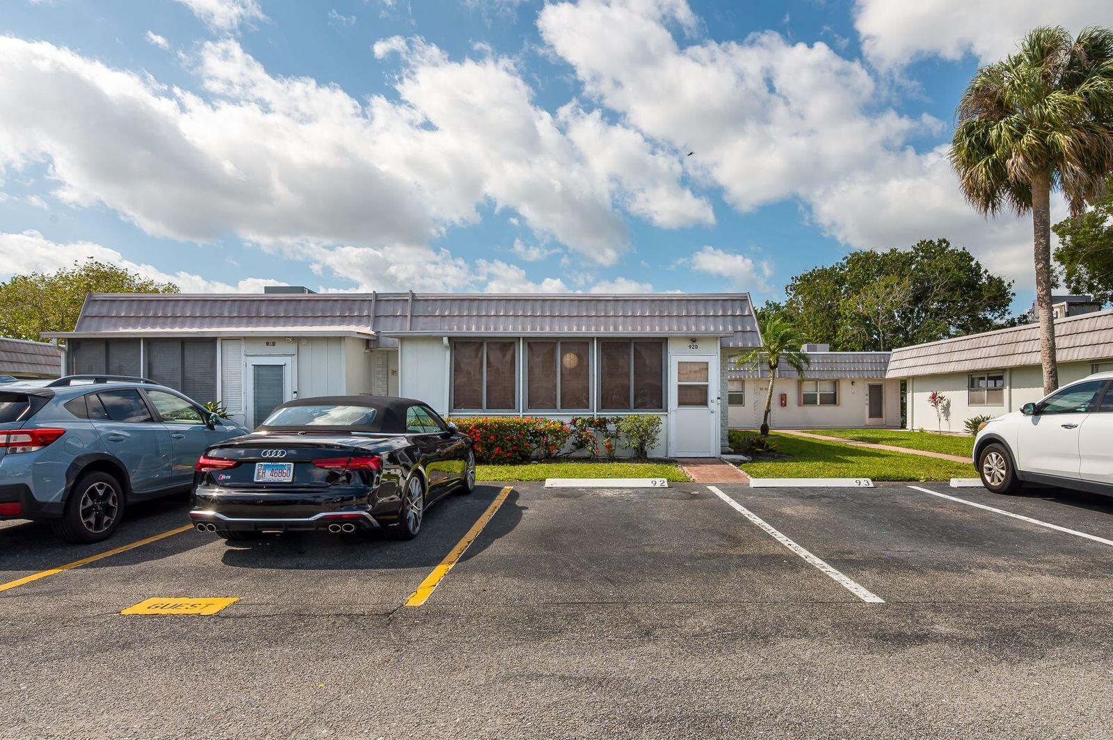 Exterior view of single-story apartment units with parking spaces in front under a blue sky — 92 Valencia Drive # D, Delray Beach FL 33446, DELRAY BEACH, FL
