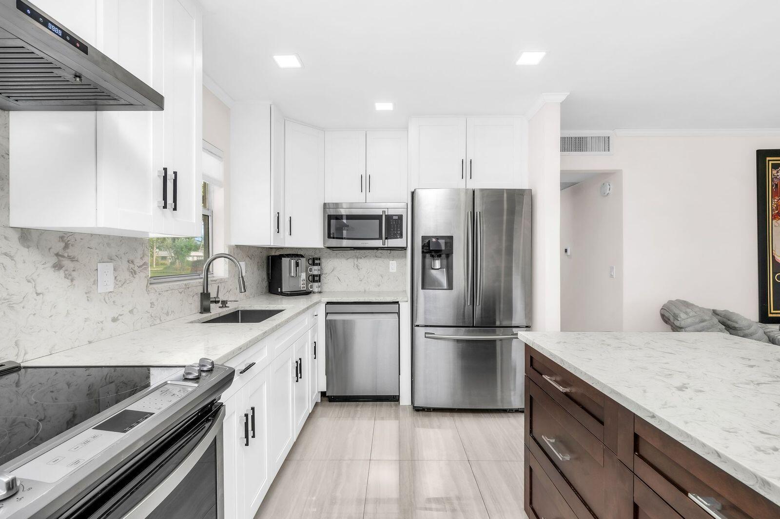 A modern kitchen features white cabinets, stainless steel appliances, and a dark wood kitchen island — 92 Valencia Drive # D, Delray Beach FL 33446, DELRAY BEACH, FL