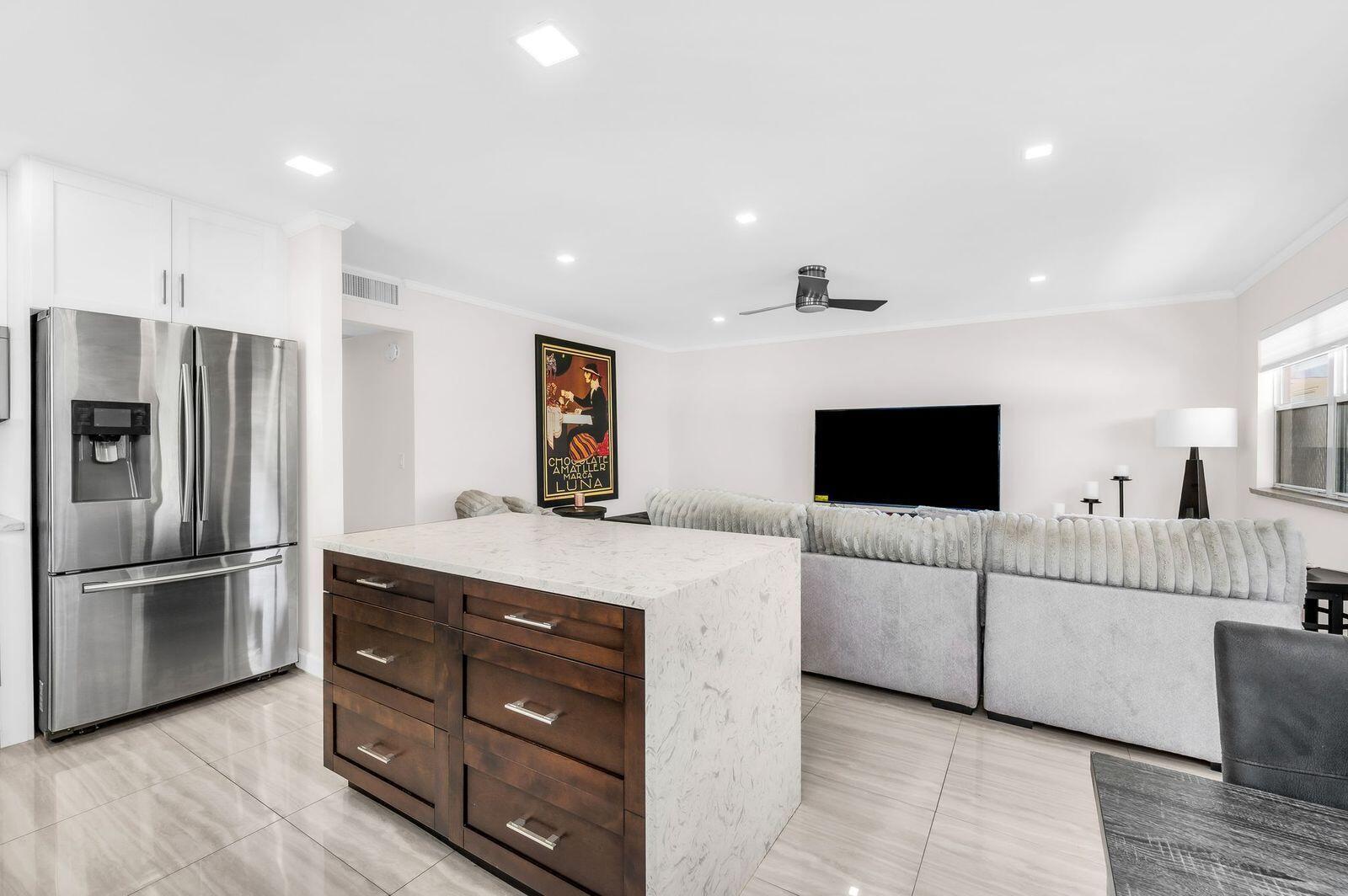 A kitchen island with a marble countertop sits in front of a living room area — 92 Valencia Drive # D, Delray Beach FL 33446, DELRAY BEACH, FL