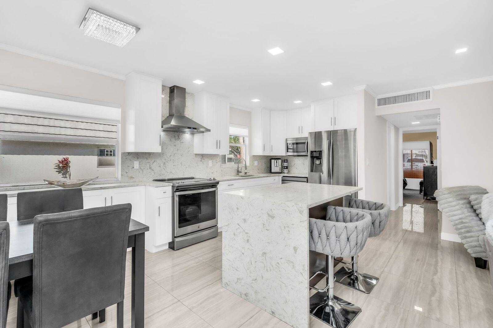 A modern kitchen features white cabinets, a marble-patterned island, stainless steel appliances, and tile flooring — 92 Valencia Drive # D, Delray Beach FL 33446, DELRAY BEACH, FL
