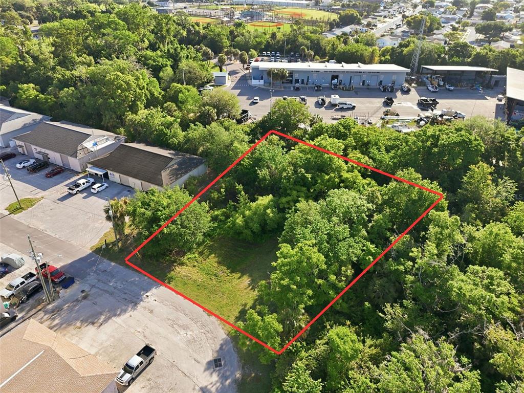 An aerial view shows a vacant, tree-covered rectangular lot outlined in red next to buildings — 7810 CLARK MOODY BOULEVARD, PORT RICHEY, FL