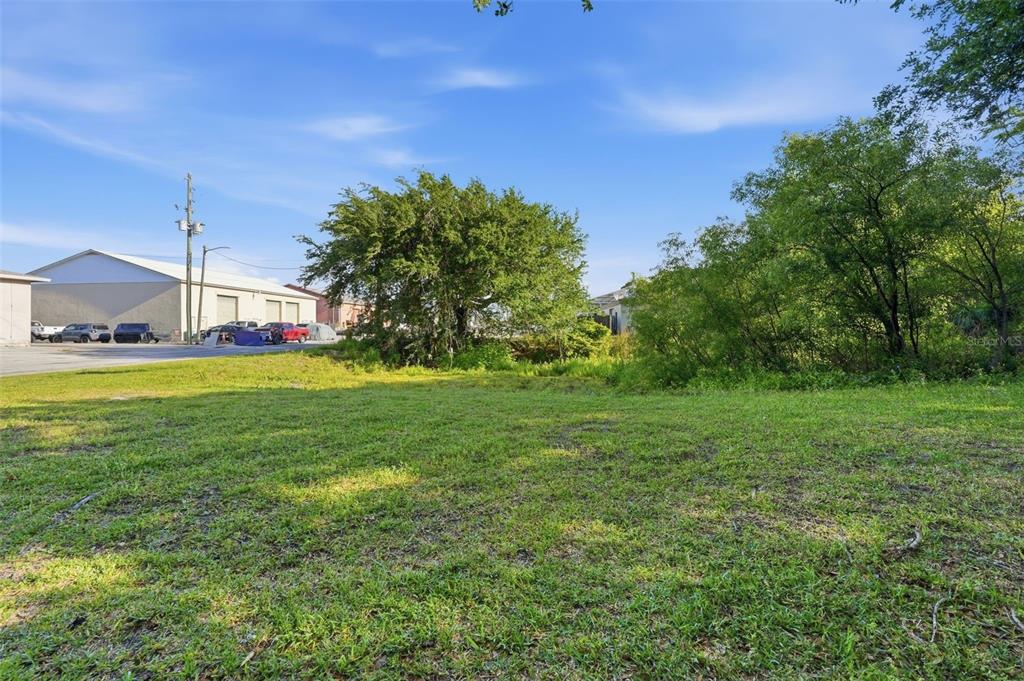 A grassy, vacant lot sits in front of trees and a commercial building — 7810 CLARK MOODY BOULEVARD, PORT RICHEY, FL