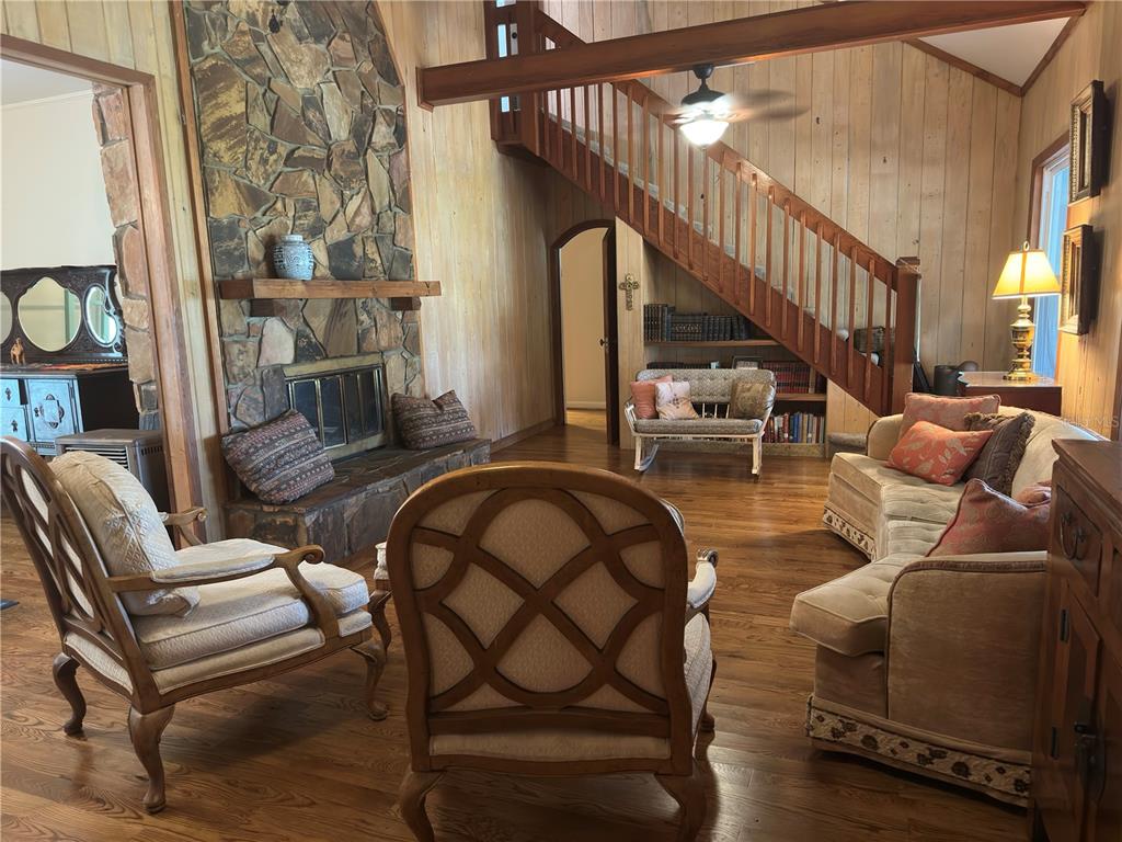 A rustic living room features a stone fireplace, wood-paneled walls, and a wooden staircase — 3900 CHALET SUZANNE DRIVE, LAKE WALES, FL