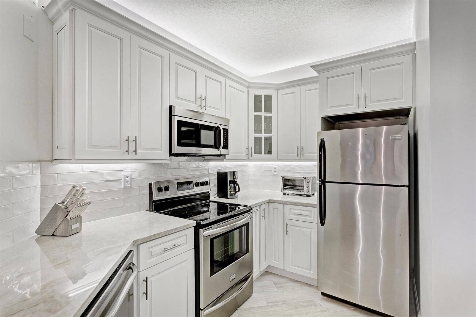 A kitchen with white cabinets, stainless steel appliances, and light-colored countertops — 500 Uno Lago Drive # 402, Juno Beach FL 33408, JUNO BEACH, FL