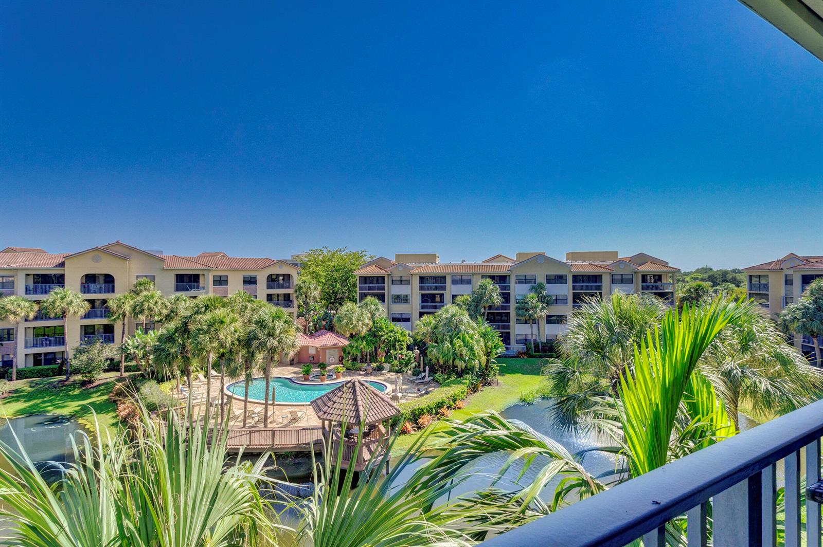 An elevated view of a swimming pool, gazebo, and pond surrounded by multi-story apartment buildings — 500 Uno Lago Drive # 402, Juno Beach FL 33408, JUNO BEACH, FL
