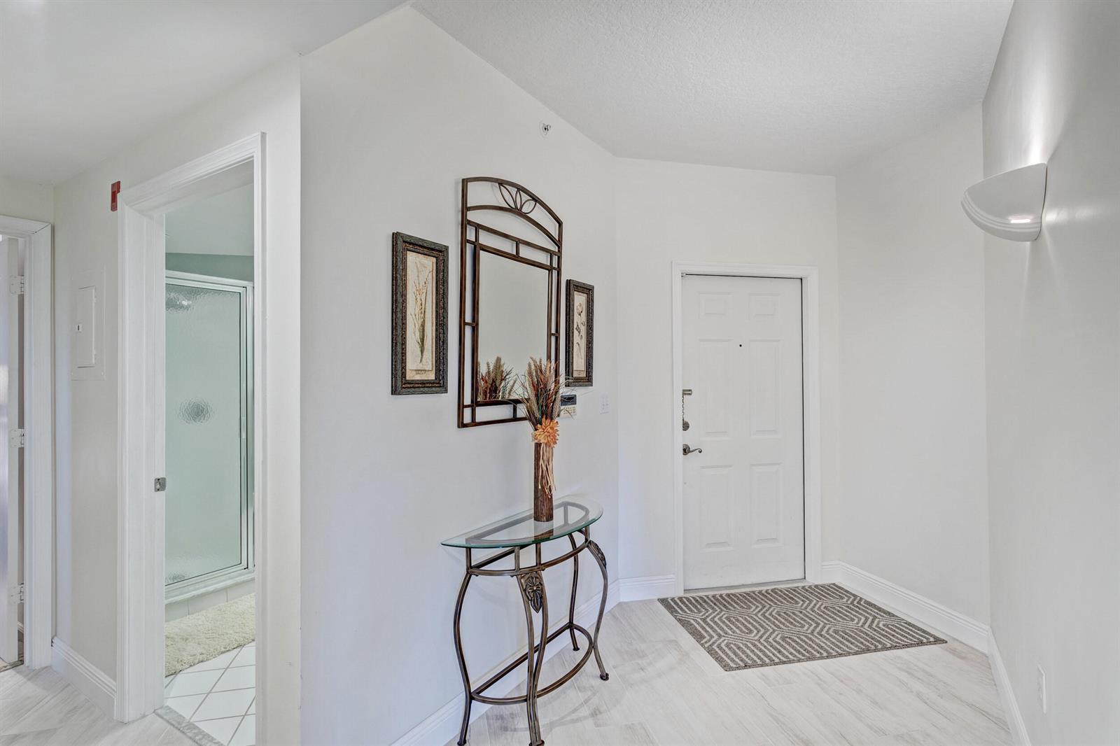 An entryway features a glass-topped console table, a wall mirror, and a white front door — 500 Uno Lago Drive # 402, Juno Beach FL 33408, JUNO BEACH, FL