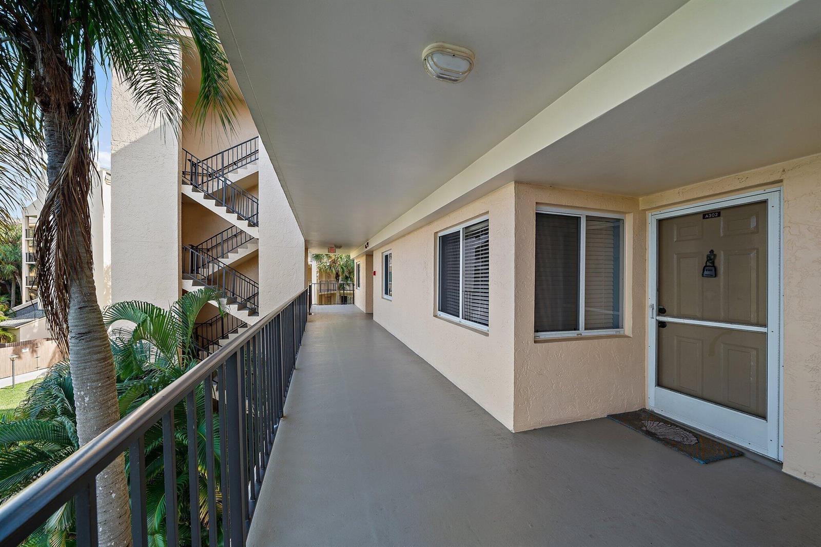 An exterior walkway leads to the entrance of a residential unit with a brown door — 275 Palm Avenue # A302, Jupiter FL 33477, JUPITER, FL