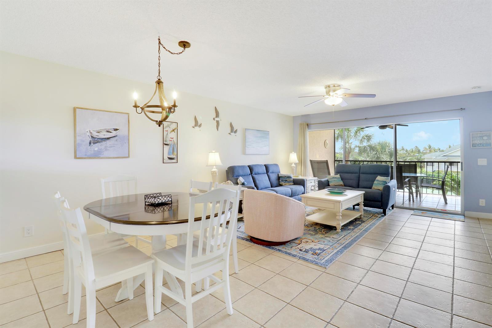 A dining area and living room with tile floors, blue sofas, and a balcony view — 275 Palm Avenue # A302, Jupiter FL 33477, JUPITER, FL