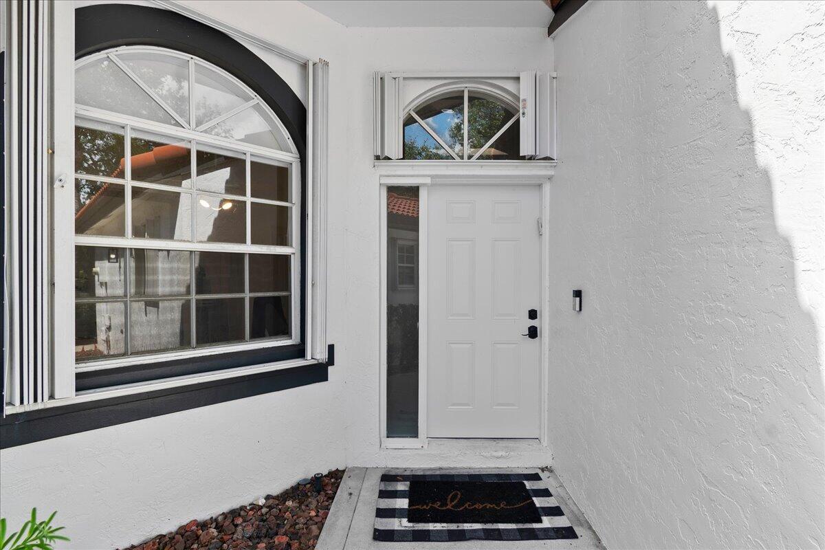 A white front door with a sidelight and arched transom window sits under a porch — 8304 Vía Di Veneto, Boca Raton FL 33496, BOCA RATON, FL