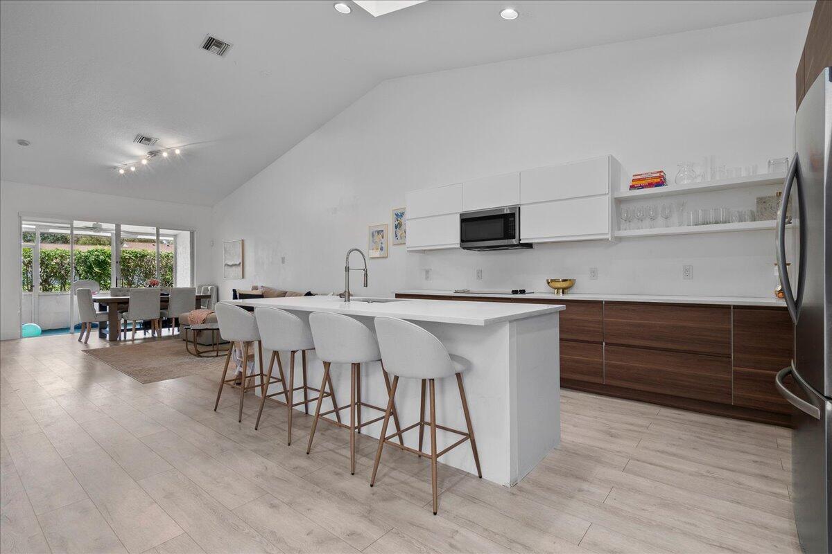 A modern kitchen features a white island with bar stools, wood cabinets, and white countertops — 8304 Vía Di Veneto, Boca Raton FL 33496, BOCA RATON, FL